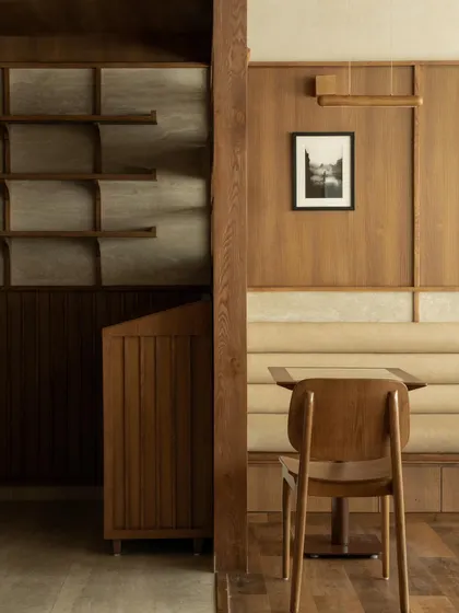Seating nooks at QBF Coffee, where I used built-in banquettes and travertine wall panels to create comfortable, intimate zones. The large windows connect these serene interiors with the greenery outside.