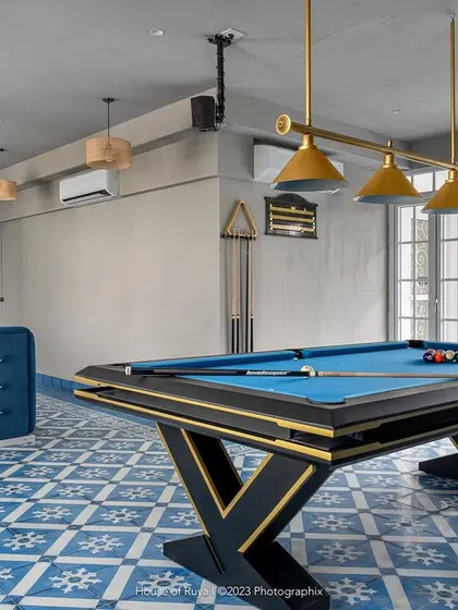 The terrace lounge is the nucleus of recreation in 'Mina Nivas'. The vibrant Aegean blue Athangudi tiles are the star of the show, creating a dynamic floor that pairs beautifully with the cement-textured walls and a modern pool table. It's a space designed for fun and gatherings.