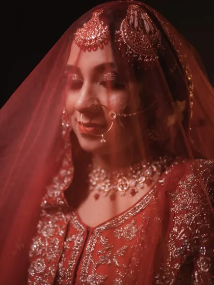 A bride is incomplete without her veil. This artistic shot through the red dupatta highlights the delicate jewelry and soft, glowing makeup underneath.