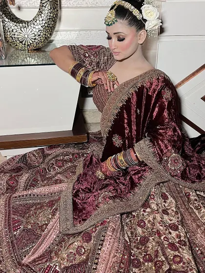 A bride seated gracefully in a deep wine-colored velvet lehenga, showcasing its rich texture and intricate embroidery.