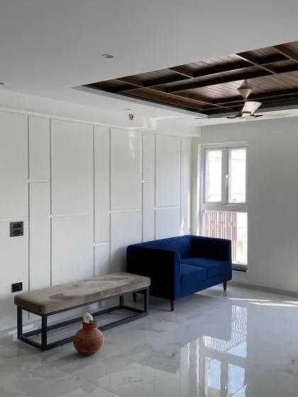 A minimalist living space in progress, featuring a custom bench and a small blue sofa. The wall is detailed with modern paneling, creating a clean and structured look.