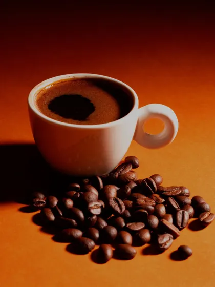 A minimalist shot of a cup of black coffee and scattered beans. The warm, gradient lighting creates a rich and inviting mood.