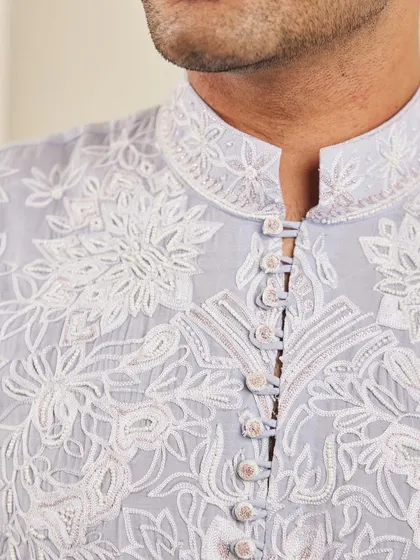 A close-up of the neckline of the lavender kurta, showing the detailed floral embroidery and fabric-covered buttons.