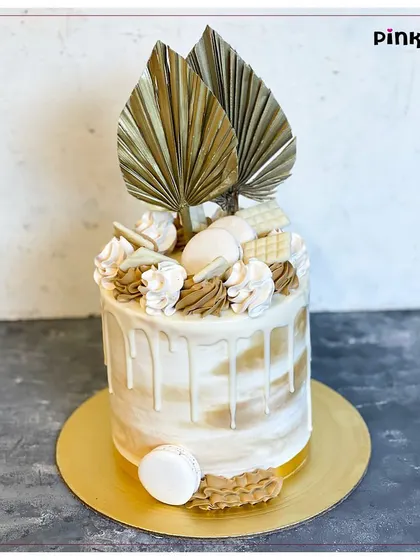 A rustic-chic design featuring a semi-naked cake with a white chocolate drip, topped with macarons, white chocolate pieces, and dried palm leaves. Perfect for a stylish, modern event.