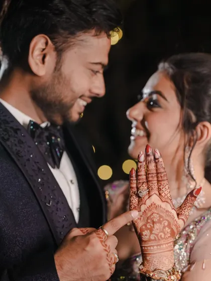 A playful moment where the groom points to the engagement ring on the bride's henna-covered hand, celebrating their union.