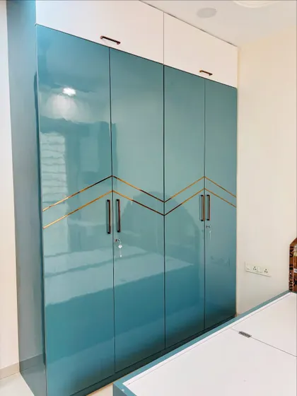 This high-gloss teal wardrobe features a striking zig-zag pattern in a gold finish, turning a simple storage unit into a statement piece.