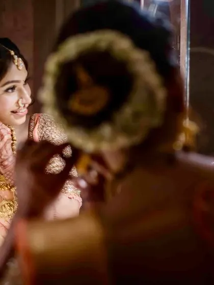 A creative shot using reflections. The bride is seen getting ready in the mirror, her reflection clear and smiling, capturing the final touches.