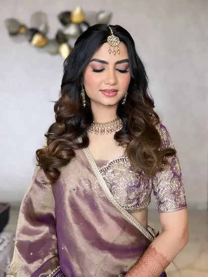 A beautiful engagement look featuring soft smokey eyes with purple hues and a radiant base. The maang tikka and jewellery are perfectly highlighted by the elegant makeup.