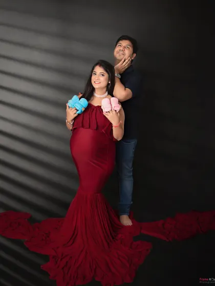 A playful and creative maternity photo. The mom-to-be holds up one pink and one blue bootie, adding a fun "guess what it will be" element to her shoot.