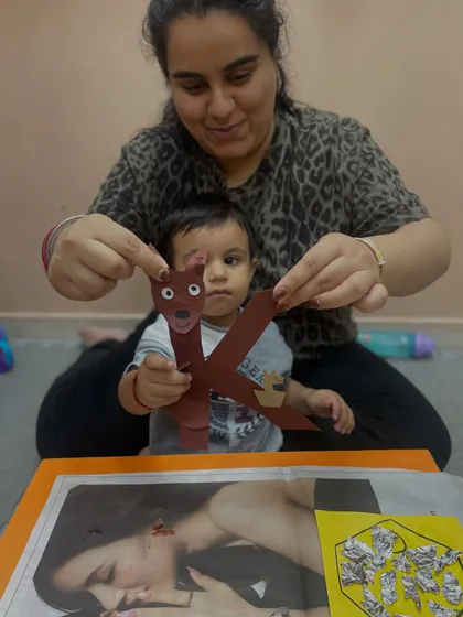 A mother helps her child assemble a paper craft shaped like the letter 'K'. This hands-on approach makes alphabet learning fun and interactive.
