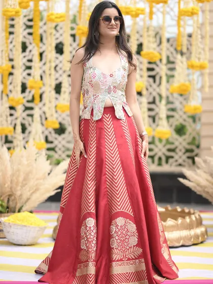 A client looking radiant at her Sagan ceremony in a custom red brocade lehenga paired with a modern, embroidered peplum-style top.