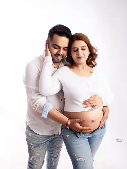 An intimate bare-bump shot with the couple dressed in casual jeans and white tops. This pose highlights their connection and the shared excitement of feeling the baby.