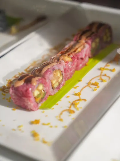 Another one of our creative sushi rolls, this one featuring a vibrant pink rice and a decorative sauce pattern. We believe every detail on the plate matters.