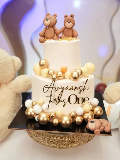 An adorable teddy bear cake for a first birthday, decorated with edible gold balloons.