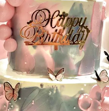Detail of a beautiful birthday cake with a gold 'Happy Birthday' topper and delicate butterfly decorations.