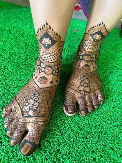 The lotus and jhumka leg design, photographed on a bright green background. The contrast makes the henna design stand out beautifully.
