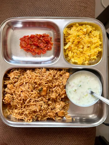 A flavorful chicken biryani served with sautéed cabbage, tomato chutney, and raita for a complete and satisfying meal.
