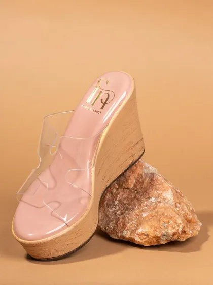 A product-only shot of a clear wedge sandal, creatively propped against a rock. This artistic composition highlights the shoe's unique design and silhouette.