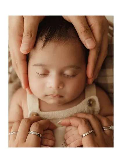 A symbolic photo with parents' hands gently holding their newborn's head, showcasing their wedding rings.