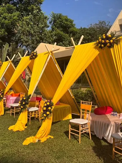 Bright yellow draped cabanas provide stylish and comfortable seating for guests at this outdoor Haldi function. It's a practical and aesthetic solution for a sunny day.