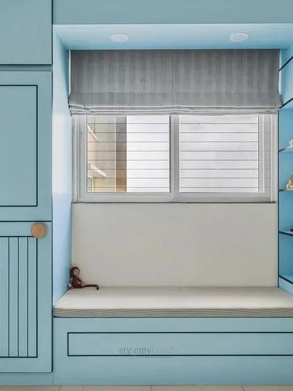 The cozy window seat in this kids' room is flanked by grooved blue wardrobes with a sleek black outline, adding a stylish contrast and depth to the design.