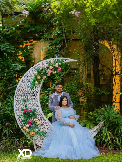 A beautiful couple's portrait on the floral crescent moon prop, set against a lush garden backdrop.