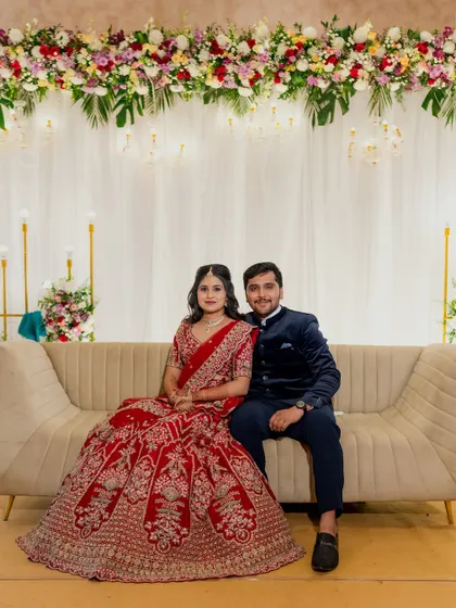 A lovely couple posing at their engagement. The stage is simple and elegant, with a white drape backdrop, a beautiful overhead floral arrangement, and modern gold candelabras.