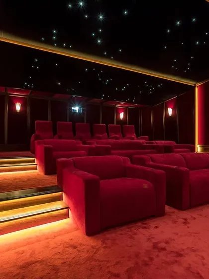 A magnificent red-themed cinema room featuring a combination of plush sofas and tiered seating. The design is elevated by a full starlight ceiling and warm, indirect lighting along the steps and walls, creating a truly luxurious viewing environment.