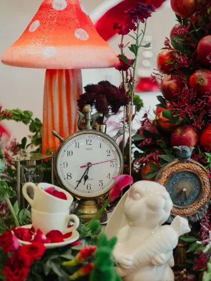 A detailed centerpiece featuring a vintage clock, stacked teacups, a white rabbit, and an apple tree, referencing key elements from the story.