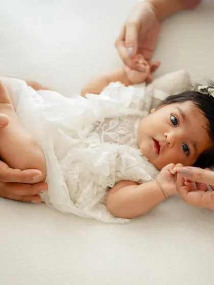A parent's hands gently holding their baby's legs and hands. This shows the scale of how tiny she is in these first few weeks.