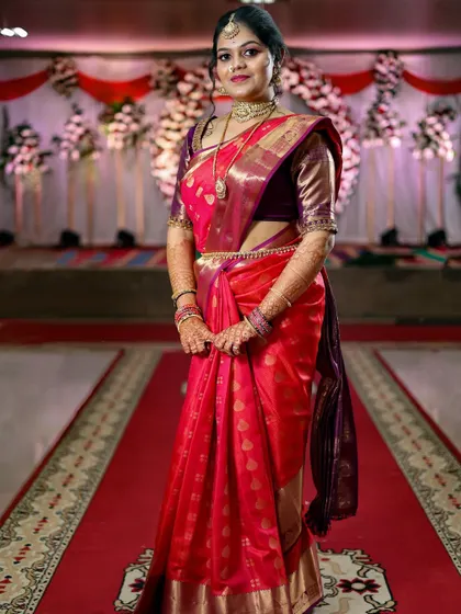 A full-length portrait of the bride in her stunning red silk saree, standing on the red carpet aisle. This shot captures the complete bridal look in all its glory.
