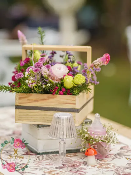 A small wooden crate filled with a beautiful assortment of flowers, part of the rustic and whimsical table decor.