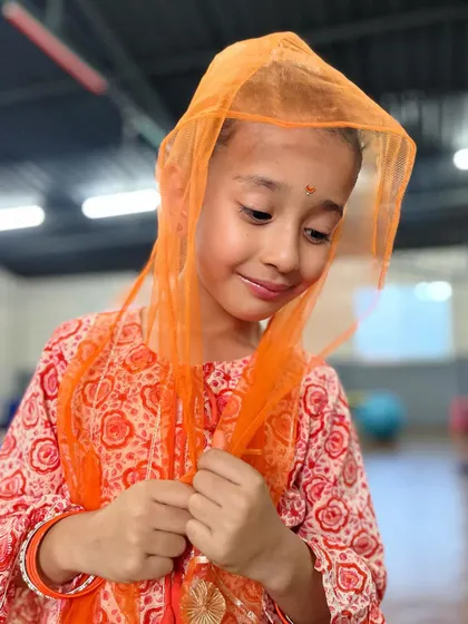 A moment of shy charm. This student looks lovely in her traditional orange outfit, showcasing a different side of her personality.