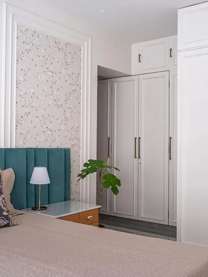 This grandparents' room emphasizes neutral colors, simplicity, and elegance. A champagne gold floral wallpaper and a teal green headboard create a sophisticated bed wall, while the white wardrobes with moulding add a perfect sheen to the space.