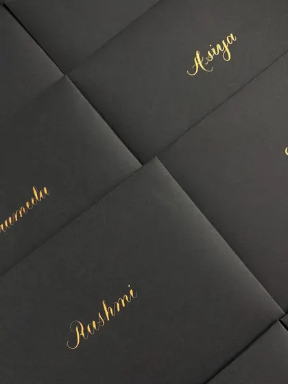 A grid of matte black envelopes, each hand-addressed with a guest's name in stunning gold calligraphy. This creates a powerful and luxurious first impression for any event.