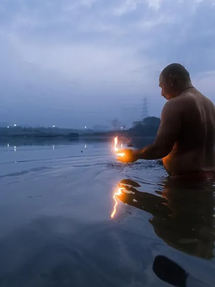 A man performs a solitary ritual with a lamp in the Yamuna river at dawn, a quiet moment of personal devotion.
