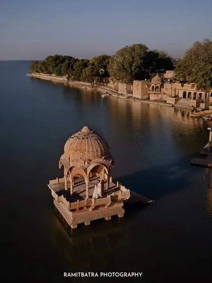 A breathtaking aerial shot of a couple standing in a cenotaph seemingly floating on Gadisar Lake in Jaisalmer, a truly magical pre-wedding moment.