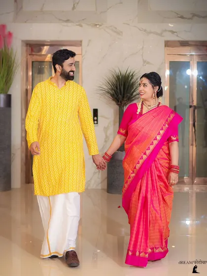 Kishi and Aaditya walking hand-in-hand, sharing a smile, dressed in vibrant traditional South Indian attire.