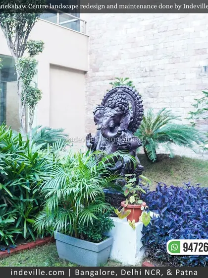 A serene garden corner at Manekshaw Centre featuring a beautiful Ganesha statue nestled among lush greenery and sculpted trees.