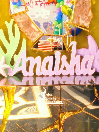 A custom-made name sign for "Anaisha" in pastel pink, decorated with a starfish and seashell. This personalized decor piece was a beautiful addition to the gift table.