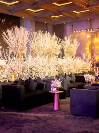 A lounge area with black sofas is backed by a massive installation of dried white and gold foliage.