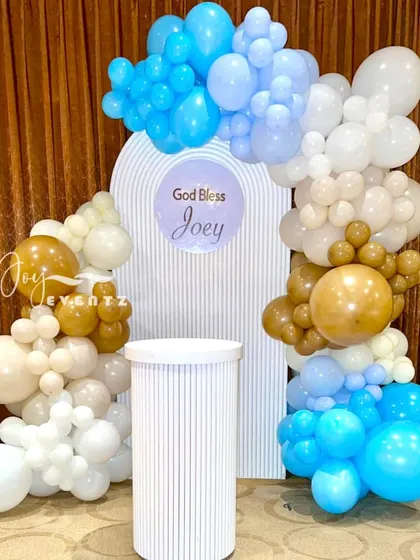 A simple and sweet stage decoration for a First Holy Communion. We used a balloon arch in shades of blue, brown, and white to frame a personalized backdrop and a single white plinth.