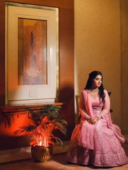 A full-length portrait of the bride seated, her pink lehenga spread beautifully around her. Her calm and poised expression creates a serene and elegant bridal photo.