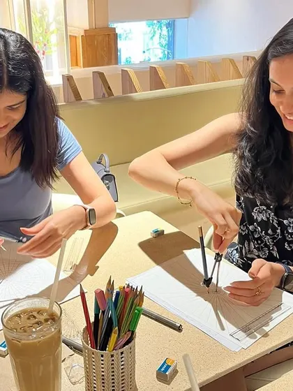 Two participants focused on getting their mandala grids just right. It's wonderful to see people enjoy the process of learning and creating together at a cafe workshop.