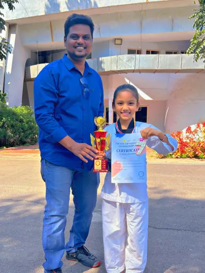 This young champion proudly displays her trophy and medal after a successful Taekwondo competition.