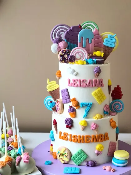 A two-tiered Candyland cake, overflowing with handcrafted edible sweets, lollipops, and ice cream cones.
