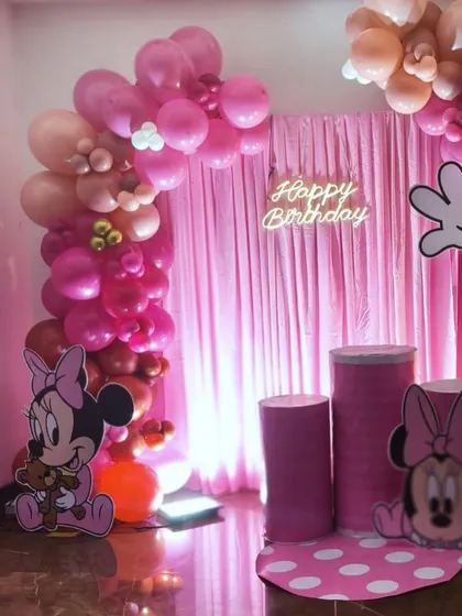 A closer look at the details of the Minnie Mouse party setup. You can see the neon "Happy Birthday" sign, the custom-wrapped pedestals for the cake, and the organic balloon arch with varying shades of pink.