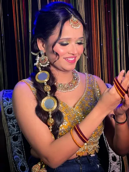 A beautiful shot of a client ready for a Mehendi or Haldi ceremony. The look features shimmery green eyeshadow, a parandi in her hair, and a bright, happy smile.