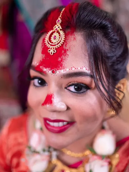 A bright and happy portrait of a Bengali bride, her face adorned with sindoor, smiling for the camera.