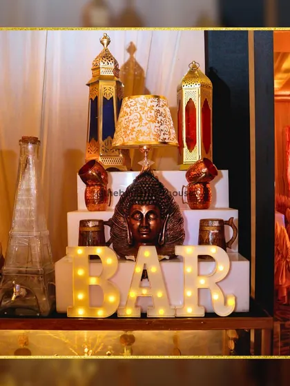 An elegant and sophisticated bar setup. The serene Buddha head, designer lanterns, and illuminated 'BAR' sign create a fusion of tranquility and modern style.